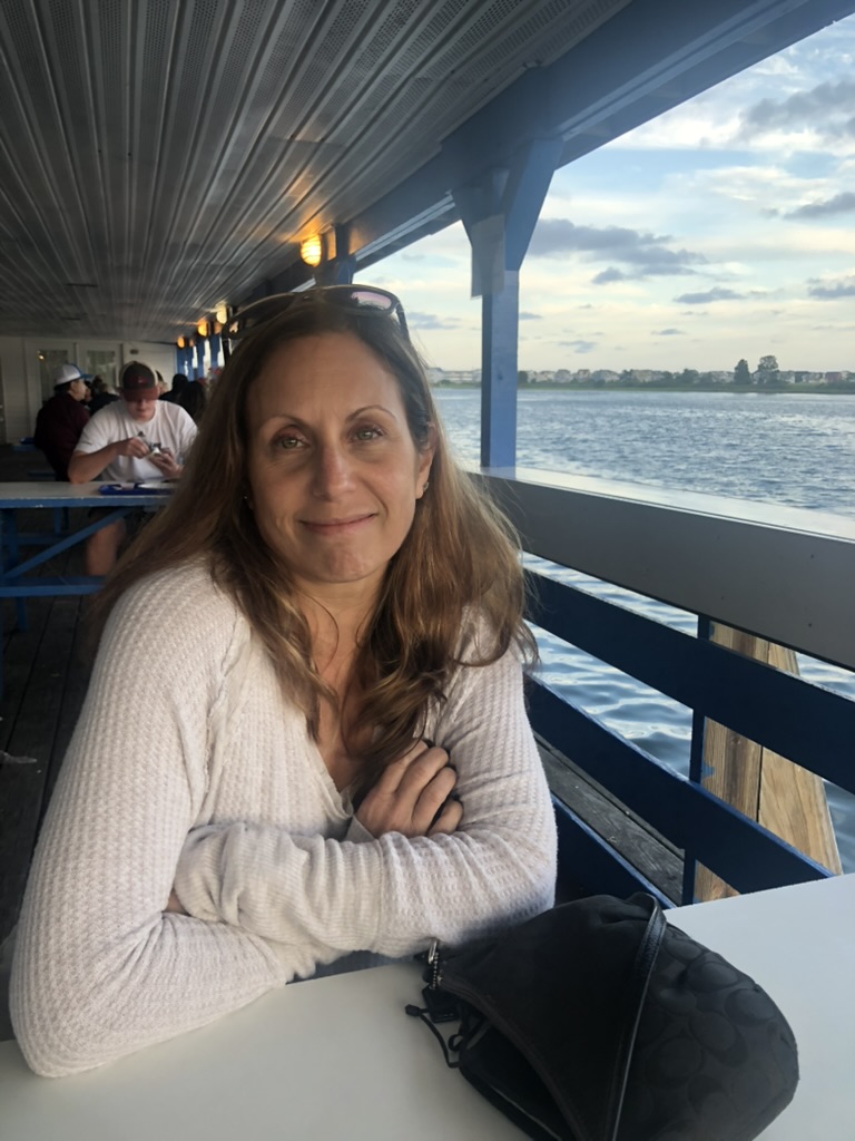 A senior woman artist smiling in a cozy, light-filled balcony
