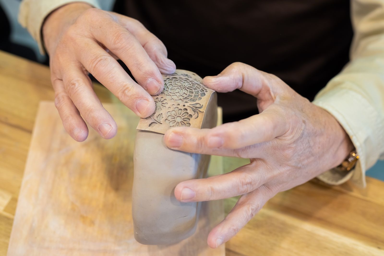 Close-up of hands decorating a clay pot with careful brushwork
