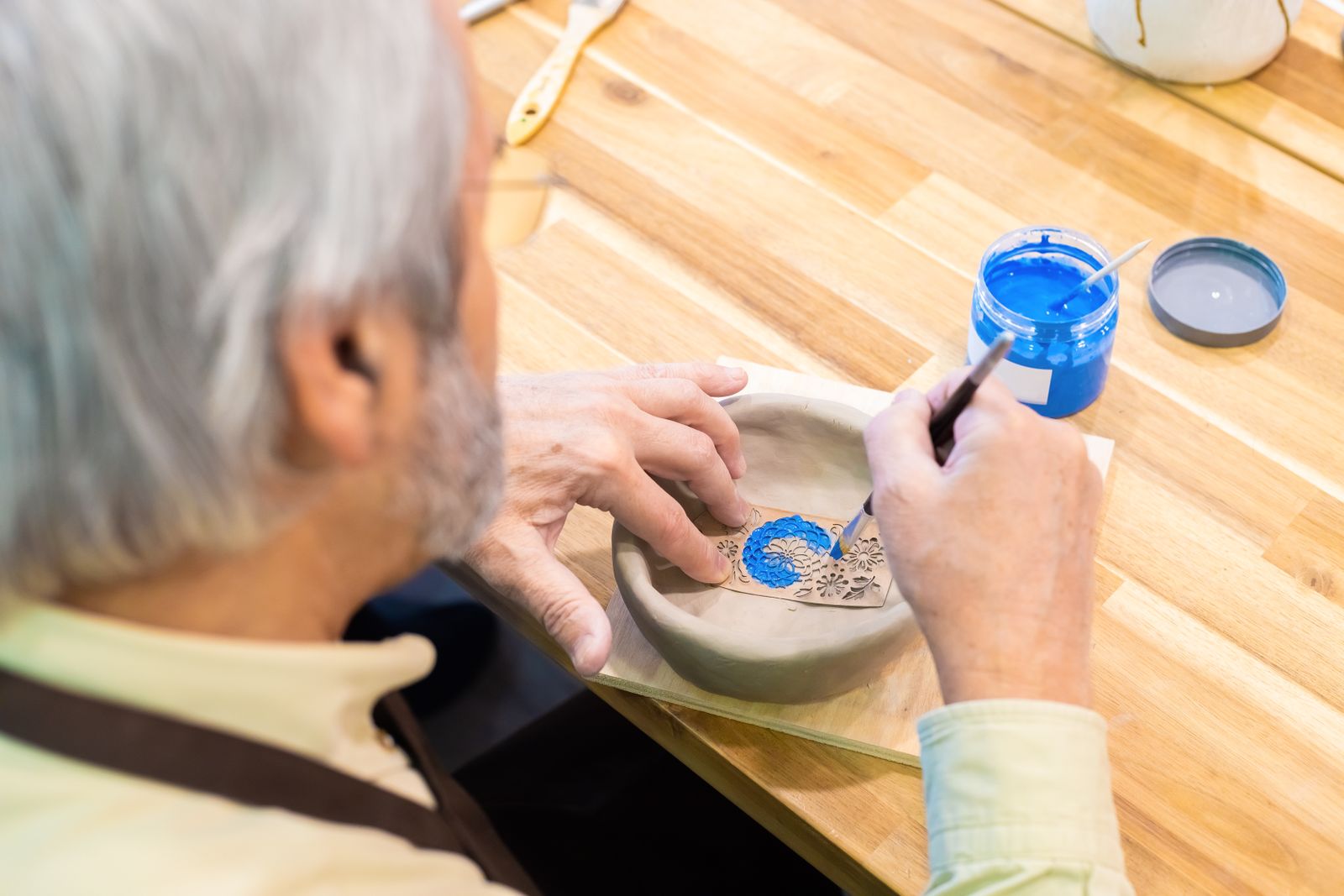 A senior man painting a ceramic bowl with blue paint