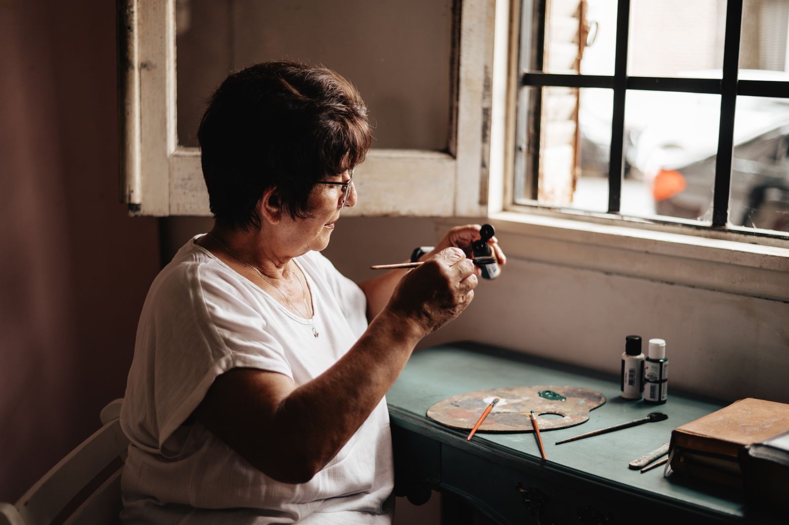 A senior woman painting by a sunlit window